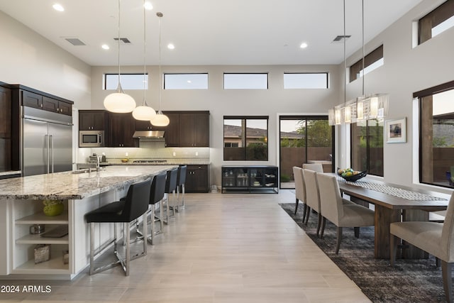 kitchen with built in appliances, tasteful backsplash, dark brown cabinets, light stone counters, and a breakfast bar area