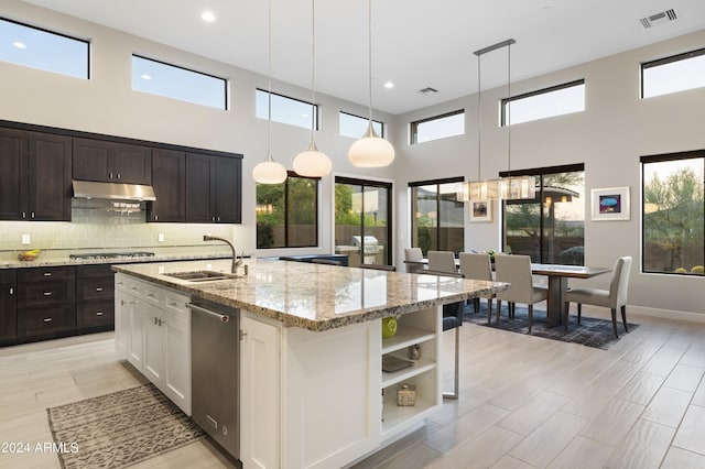 kitchen with a towering ceiling, a kitchen island with sink, sink, white cabinetry, and hanging light fixtures