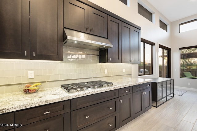 kitchen featuring light stone countertops, backsplash, a towering ceiling, stainless steel gas stovetop, and dark brown cabinets