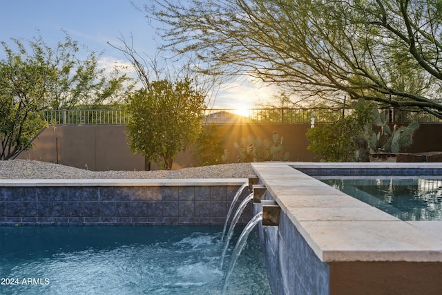 pool at dusk featuring pool water feature