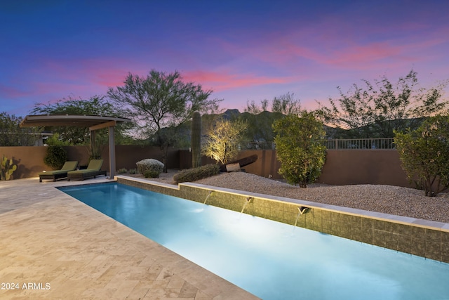 pool at dusk featuring a patio area and pool water feature