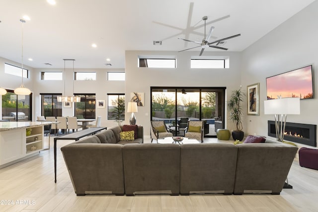 living room with ceiling fan, light wood-type flooring, and a high ceiling