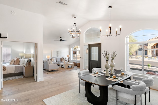 dining area with ceiling fan with notable chandelier, high vaulted ceiling, and light hardwood / wood-style floors