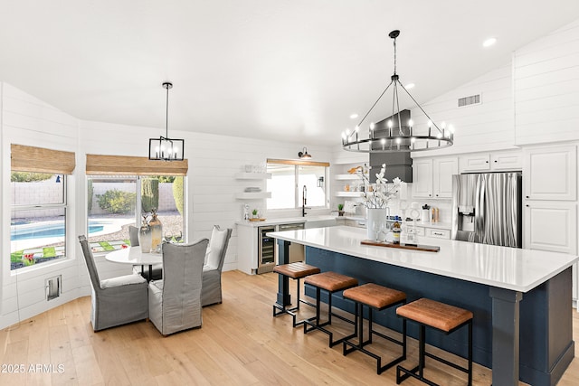 kitchen with a spacious island, stainless steel fridge with ice dispenser, a notable chandelier, light hardwood / wood-style floors, and white cabinets