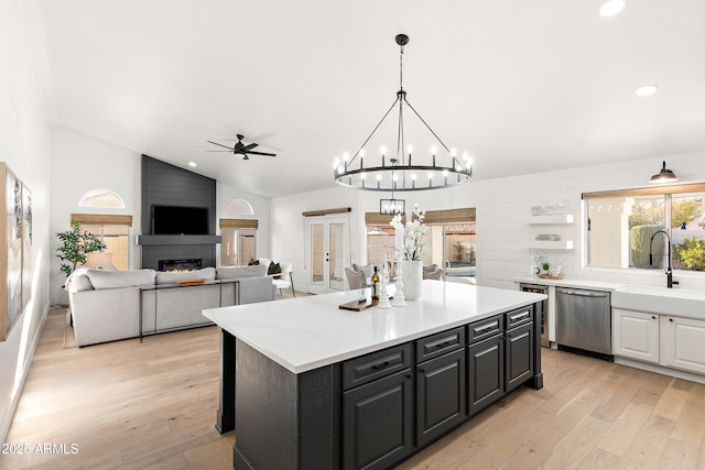 kitchen with sink, decorative light fixtures, stainless steel dishwasher, a large fireplace, and a kitchen island