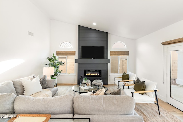 living room with vaulted ceiling, light hardwood / wood-style floors, and a large fireplace