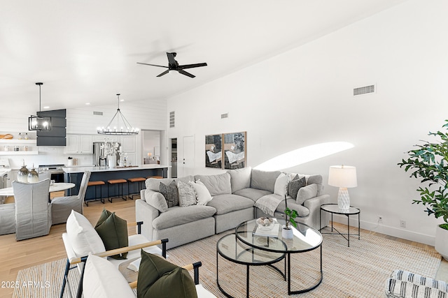 living room featuring ceiling fan with notable chandelier, high vaulted ceiling, and light hardwood / wood-style floors