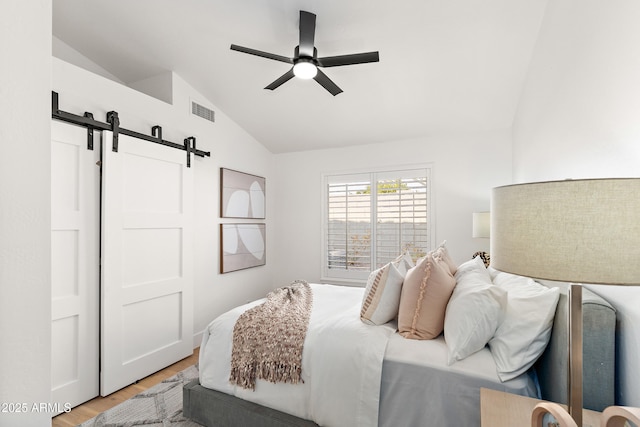 bedroom with vaulted ceiling, a barn door, hardwood / wood-style floors, and ceiling fan