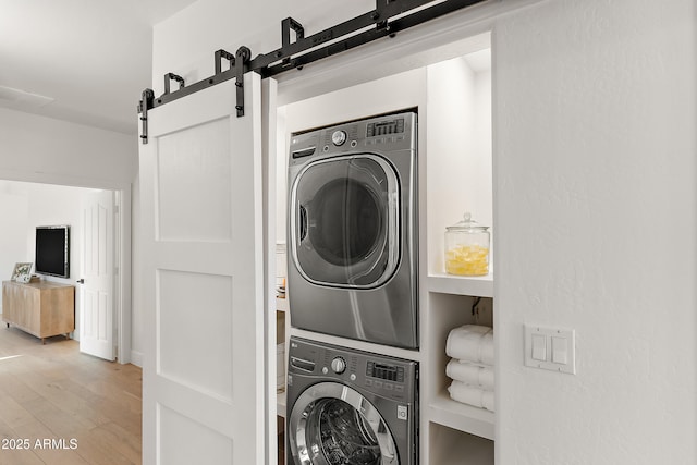 laundry area featuring stacked washer / drying machine, a barn door, and wood-type flooring