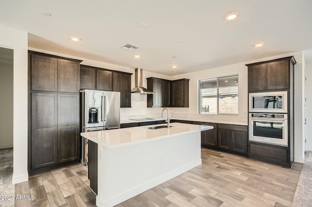 kitchen with wall chimney exhaust hood, light wood-type flooring, sink, and appliances with stainless steel finishes