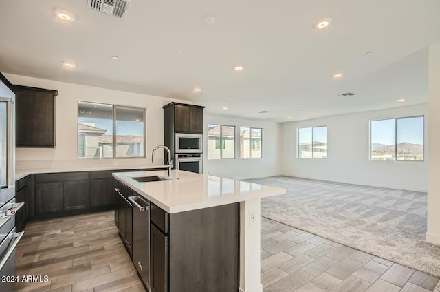 kitchen with dark brown cabinetry, stainless steel appliances, a center island with sink, and sink