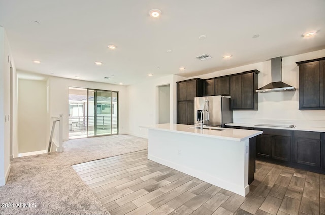 kitchen with dark brown cabinetry, sink, wall chimney exhaust hood, stainless steel fridge with ice dispenser, and a center island with sink