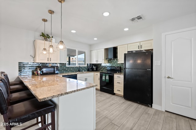 kitchen featuring pendant lighting, black appliances, a breakfast bar area, kitchen peninsula, and wall chimney range hood