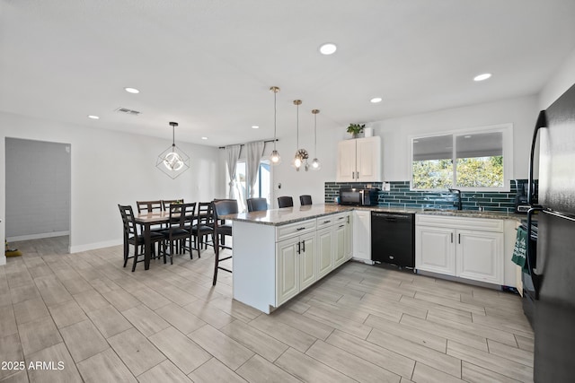 kitchen featuring hanging light fixtures, a kitchen breakfast bar, black dishwasher, kitchen peninsula, and a wealth of natural light