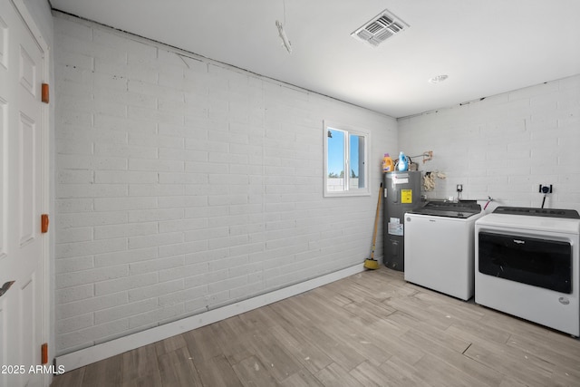 washroom with washer and clothes dryer, electric water heater, and brick wall