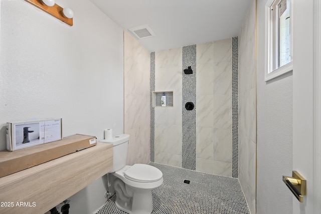 bathroom featuring tiled shower, toilet, and tile patterned flooring