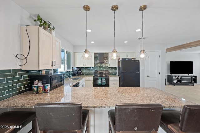 kitchen with wall chimney range hood, decorative light fixtures, black appliances, and a kitchen breakfast bar