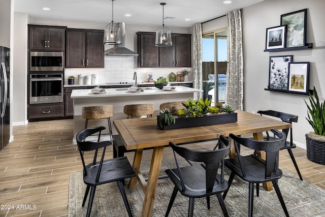 kitchen featuring wood finish floors, light countertops, dark brown cabinets, wall chimney exhaust hood, and tasteful backsplash