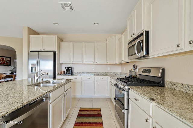 kitchen with white cabinetry, stainless steel appliances, sink, and light stone counters