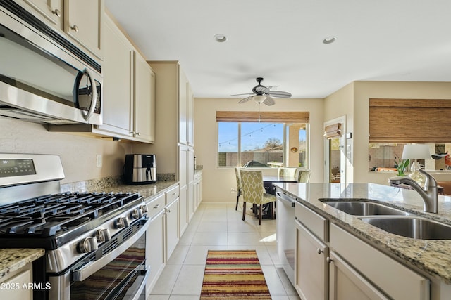 kitchen with stainless steel appliances, sink, light stone counters, and cream cabinetry