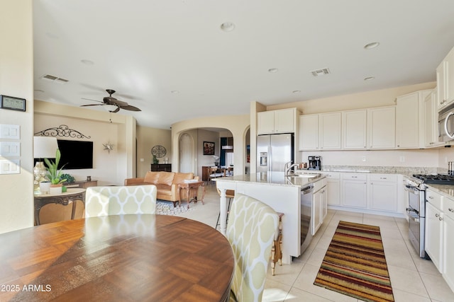 kitchen featuring appliances with stainless steel finishes, white cabinetry, sink, light stone countertops, and a center island with sink