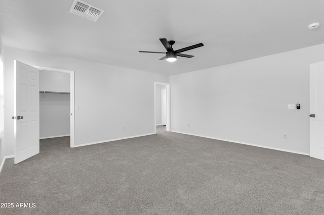 interior space with a walk in closet, a closet, dark carpet, and ceiling fan