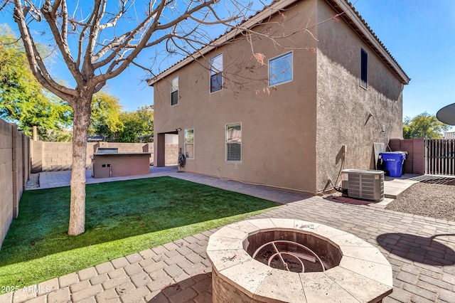 rear view of property with central AC unit, a patio area, an outdoor fire pit, and a lawn