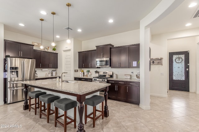 kitchen with a kitchen island with sink, sink, a kitchen breakfast bar, stainless steel appliances, and decorative light fixtures