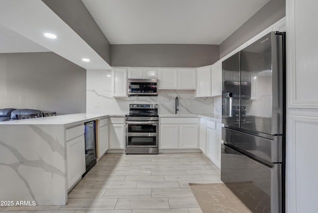 kitchen featuring wine cooler, appliances with stainless steel finishes, kitchen peninsula, decorative backsplash, and white cabinets