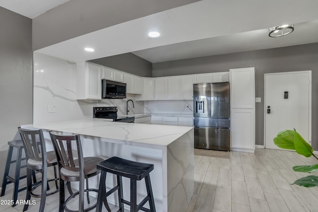 kitchen with appliances with stainless steel finishes, white cabinets, a kitchen breakfast bar, and kitchen peninsula