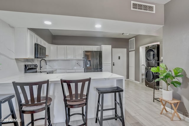 kitchen with stacked washing maching and dryer, kitchen peninsula, stainless steel fridge with ice dispenser, and white cabinets