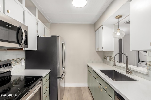 kitchen with hanging light fixtures, appliances with stainless steel finishes, stacked washer and clothes dryer, and white cabinets