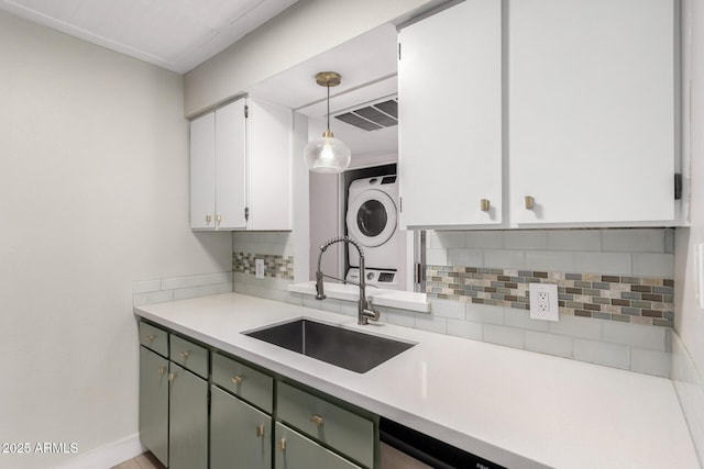 kitchen featuring sink, stacked washer and dryer, white cabinetry, backsplash, and hanging light fixtures