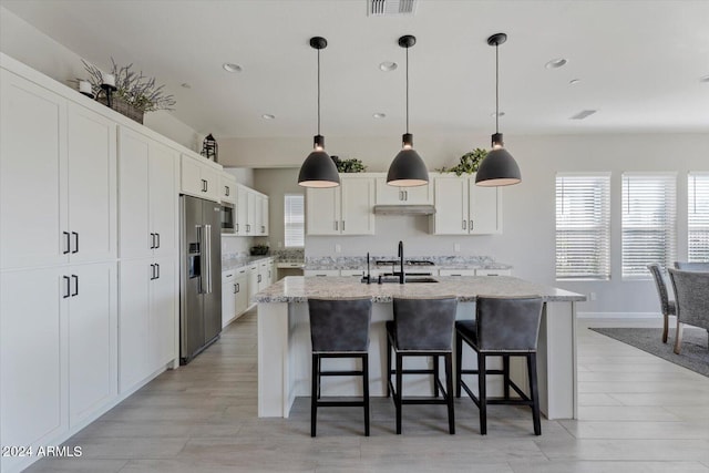 kitchen with appliances with stainless steel finishes, a center island with sink, hanging light fixtures, and white cabinets