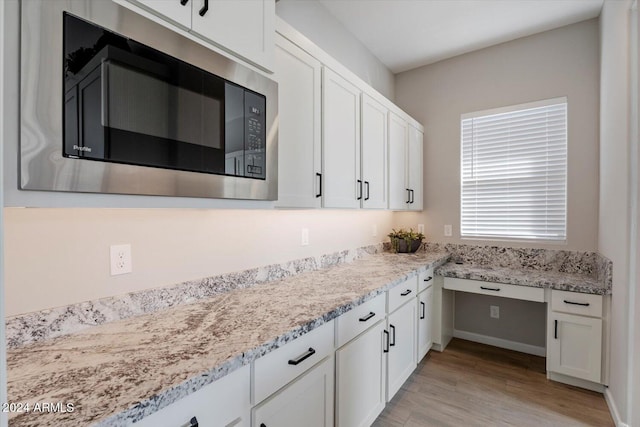 kitchen with white cabinetry, light hardwood / wood-style floors, stainless steel microwave, and light stone counters