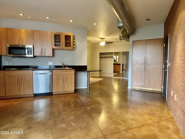 kitchen featuring ceiling fan, stainless steel appliances, sink, and brick wall