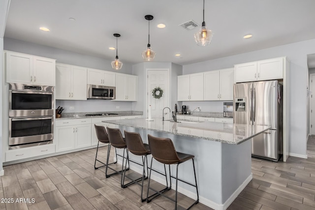 kitchen with a kitchen breakfast bar, stainless steel appliances, pendant lighting, a center island with sink, and white cabinetry