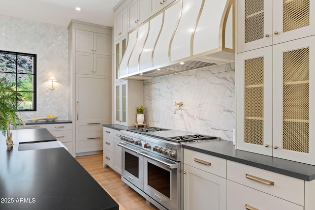 kitchen with backsplash, range with two ovens, dark countertops, and custom exhaust hood