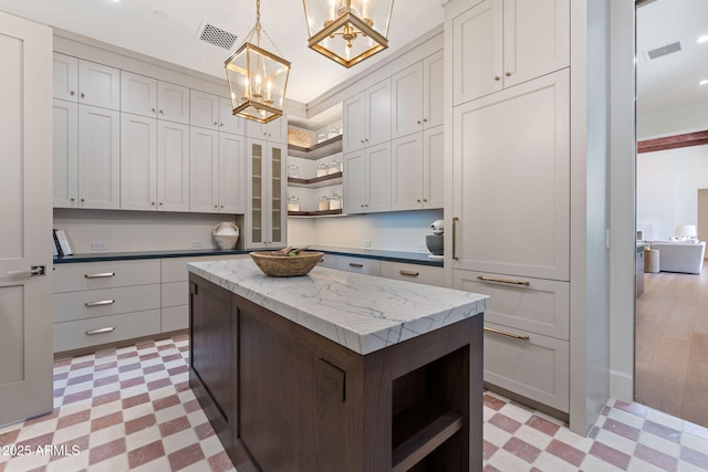 kitchen with open shelves, a chandelier, light floors, a kitchen island, and visible vents