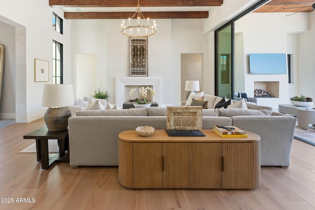 living area featuring light wood-style floors, baseboards, beamed ceiling, an inviting chandelier, and a high ceiling