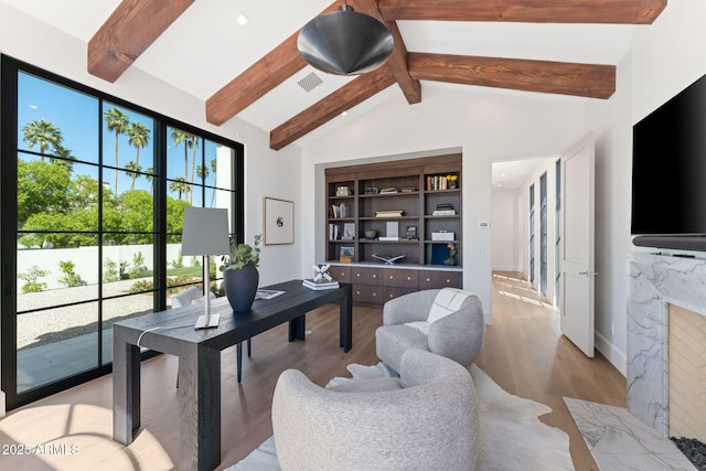 home office with visible vents, a fireplace, baseboards, vaulted ceiling with beams, and light wood finished floors