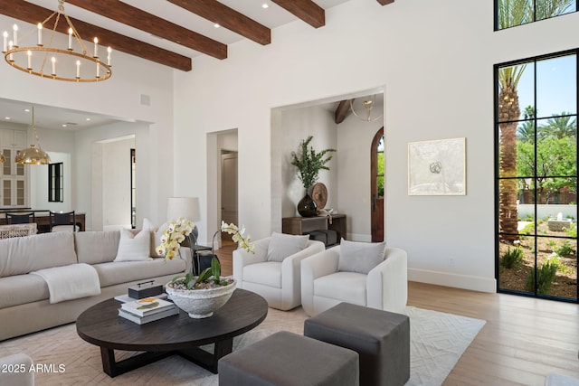living room featuring a towering ceiling, a chandelier, baseboards, light wood-type flooring, and beamed ceiling