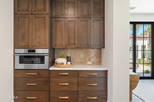 kitchen featuring light countertops, stainless steel oven, and backsplash