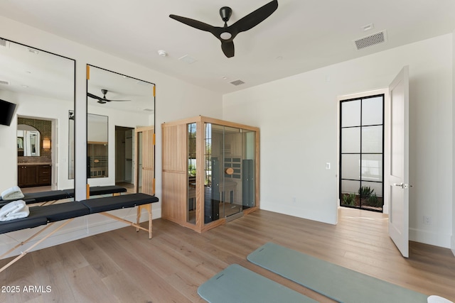 exercise room featuring ceiling fan, visible vents, wood finished floors, baseboards, and a wealth of natural light