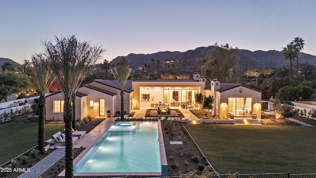 back of house at dusk with a yard, a patio, a mountain view, and stucco siding