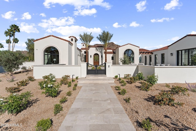 mediterranean / spanish home with a gate, a fenced front yard, a tile roof, and stucco siding