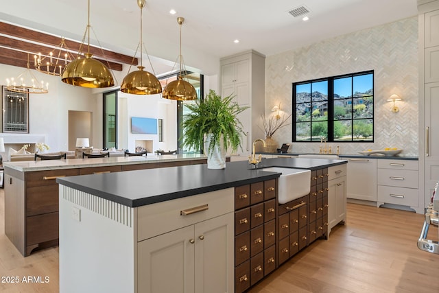kitchen featuring a large island with sink, visible vents, dark countertops, and light wood-type flooring