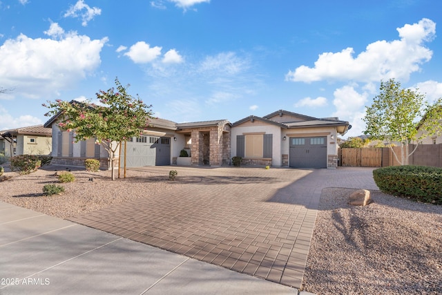 view of front of property featuring a garage, fence, stone siding, decorative driveway, and stucco siding