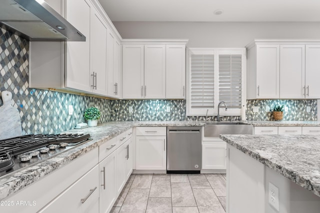 kitchen featuring stainless steel appliances, a sink, white cabinetry, wall chimney range hood, and decorative backsplash