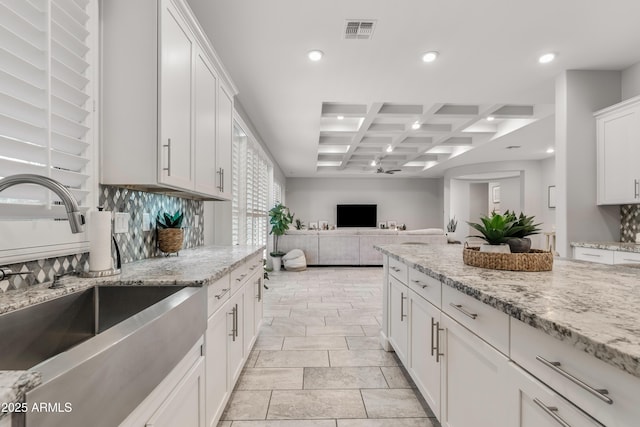 kitchen with visible vents, coffered ceiling, light stone countertops, white cabinetry, and a sink